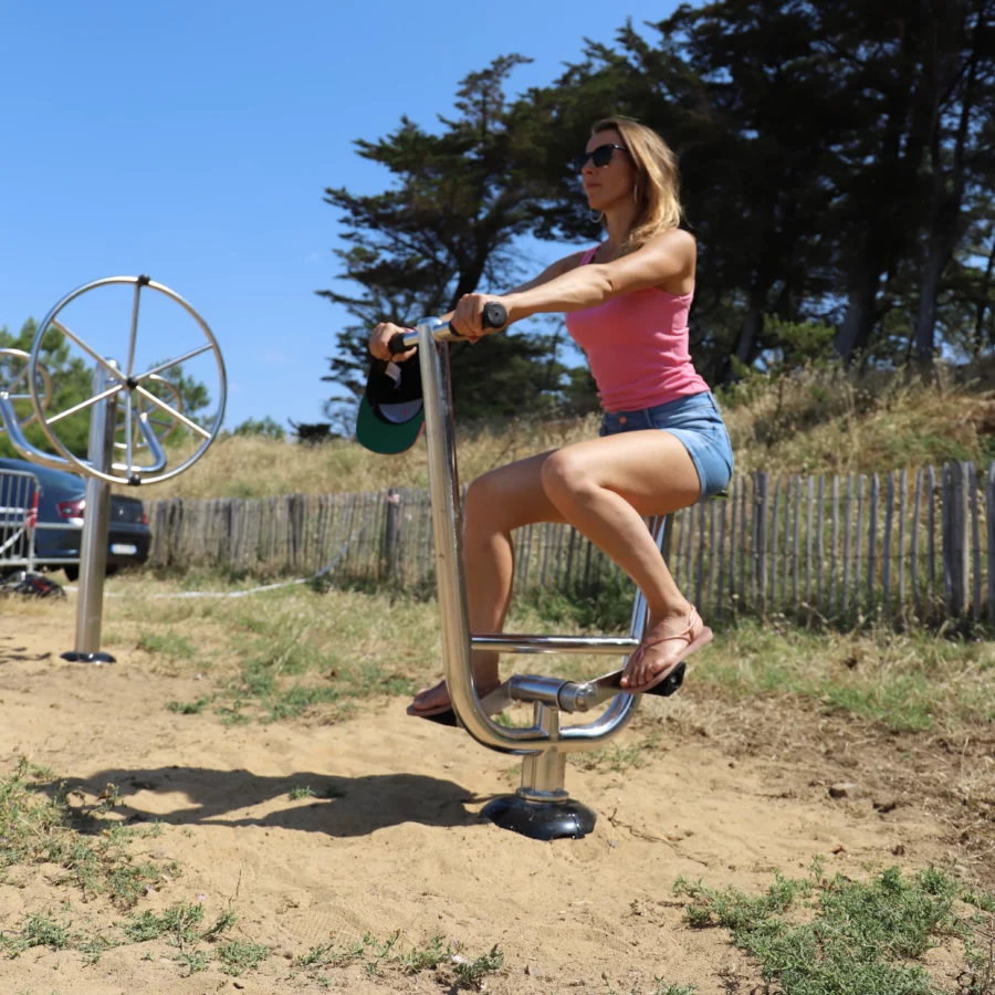 femme pédalant sur un vélo inox en bord de mer