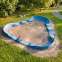 circuit de pumptrack FP9 triangulaire dans un square arboré avec des enfants en BMX et draisienne dessus